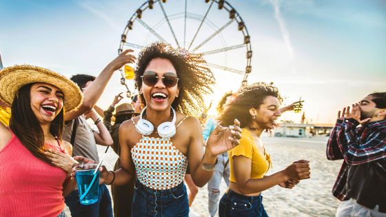 Personen tanzen auf einem Festival, im Hintergrund steht ein Riesenrad. 