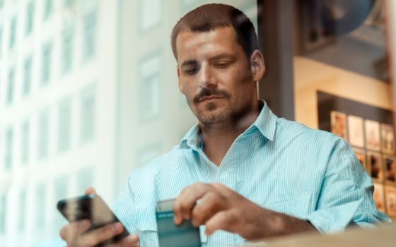 Ein Mann sitzt hinter einer Glasscheibe und schaut auf sein Smartphone.
