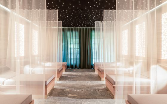 In einem Spa stehen große Holzliegen, die durch leichte Vorhänge getrennt sind, an der Decke leuchten viele kleine Lichter. 