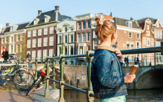 Mädchen mit Eis steht auf einer Brücke in Amsterdam und blickt auf die historischen Grachtenhäuser.