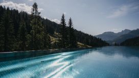 Langer Infinity-Pool inmitten einer bewaldeten Berglandschaft unter blauem Himmel.