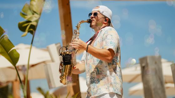 Ein Mann mit kurzem Hemd und Sonnenbrille spielt Saxophon