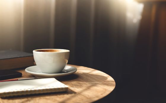Eine Tasse Kaffee und ein Notizbuch liegen auf einem Holztisch.