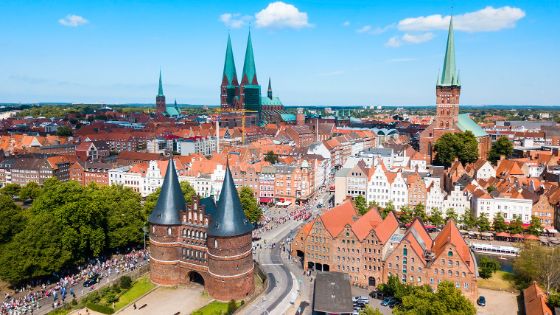 Altstadtpanorama von Lübeck mit Giebelhäusern, Backsteinkirchen und rundem Stadttor.