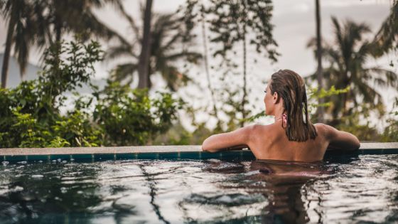 Frau in einem Pool lehnt sich am Rand an, im Hintergrund Palmen