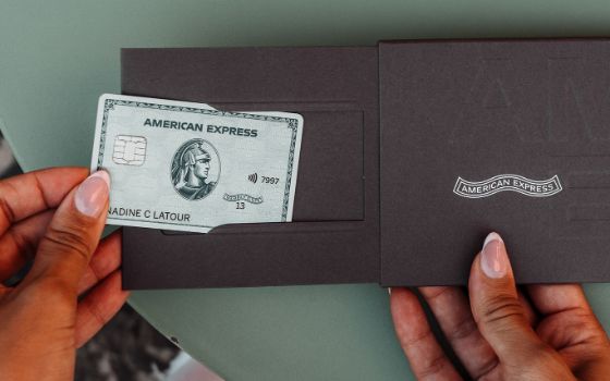 Eine Person zieht eine silberne Kreditkarte von American Express aus einem Schuber aus grauer Kartonage.