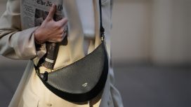 Eine Frau trägt eine schwarze Umhängetasche von der Designerin Christina Stahl und hält eine Zeitung unter ihrem Arm. 