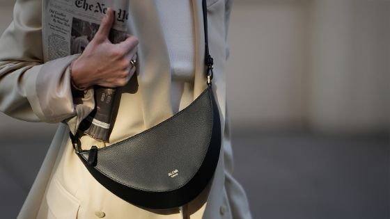 Eine Frau trägt eine schwarze Umhängetasche von der Designerin Christina Stahl und hält eine Zeitung unter ihrem Arm.