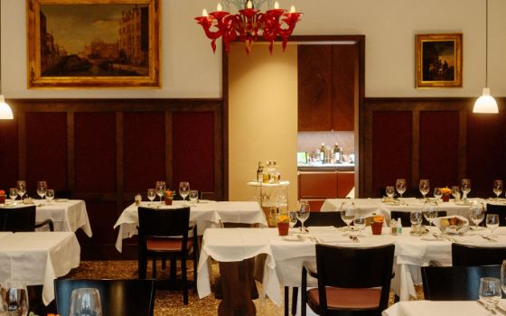 Lange, weiss eingedeckte Tische in einem stilvollen Speiseraum mit Holzelementen und Gemälden in Goldrahmen an der Wand.