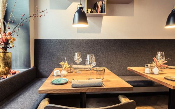 Zwei eingedeckte Holztische vor einer grauen Polsterbank in einem stilvollen Restaurant.