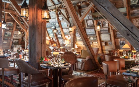 Mit Holz verkleideter Innenraum eines Restaurants in einem Dachgiebel mit vielen gedeckten Tischen, Lederstühlen und zahlreichen Bildern und Fotografien an den Dachwänden.