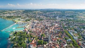 Luftaufnahme von Konstanz am Bodensee mit Altstadt, Hafen, Bahnhofsbereich und umgebender Landschaft an einem sonnigen Tag.