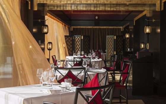 Die Veranda des Restaurants Le-Tsé-Fung in Genf mit schön gedeckten Tischen und leichten Vorhängen, die im Wind
