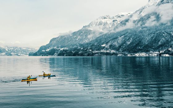 Eine Gruppe Kajaks auf einem See vor verschneiten Bergen. 