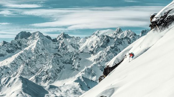 Ein Skifahrer fährt einen steilen Berghang hinunter vor schneebedecktem Gipfelpanorama.
