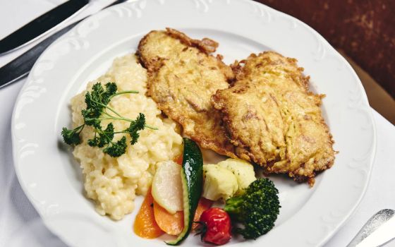 Paniertes Fleisch, Kartoffelpüree und Gemüse liegen auf einem weissen Teller.