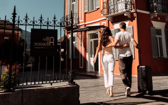 Ein Mann und eine Frau spazieren Arm in Arm auf ein romantisches, idyllisches Stadthotel zu.