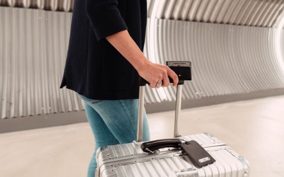 Eine Person läuft mit einem hochwertigen Aluminiumkoffer durch einen silbern verkleideten Durchgang, in ihrer Hand hält sie ein schwarzes Lederetui mit einer silbernen American Express Kreditkarte.