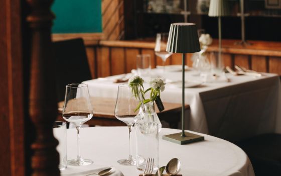 In einem Restaurant mit Holz-Elementen an den Wänden stehen zwei gedeckte Tische mit weisser Tischdecke und einer kleinen Lampe. 