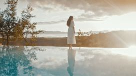 Eine Frau in einem weissen Kleid steht entspannt vor dem Swimmingpool eines stilvollen Hotels und verkörpert modernen Luxus.
