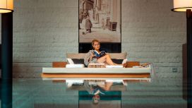 Frau entspannt am Indoor-Pool auf Liege mit Buch in modernem Designhotel, stilvolles Ambiente mit Wandkunst im Hintergrund.