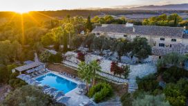 Mitten in der Natur liegt ein sandfarbenes Gebäude mit einem Swimmingpool, rundherum wachsen Bäume und Palmen. 