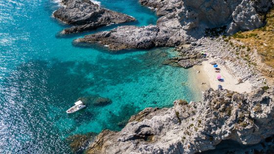 Mediterrane Felsküste mit Sandstrand in einer kleinen Bucht am türkisblauen Meer aus der Luftperspektive.