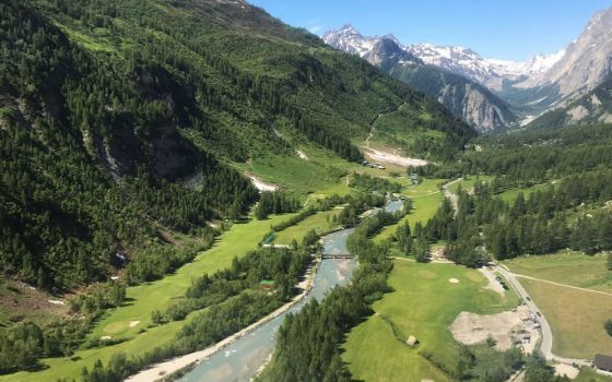 Flusstal mit Golfplatz und Waldgebiet inmitten einer Berglandschaft. 
