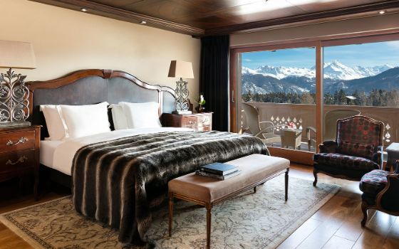 In einem Hotelzimmer steht eine grosses Bett vor einem Balkon mit Blick auf die Berge. 