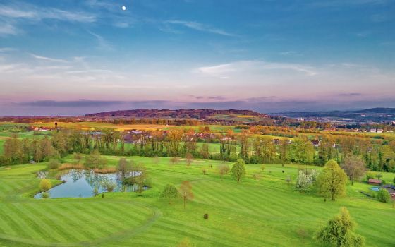 Ein Golfplatz ist umgeben Bergen, Bäumen und einem kleinen See.