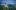 Märchenhaftes Schloss Neuschwanstein im Stil der Neuromantik auf einem bewaldeten Hügel vor mit Nebelschwaden verhangener Berglandschaft im Abendlicht. 