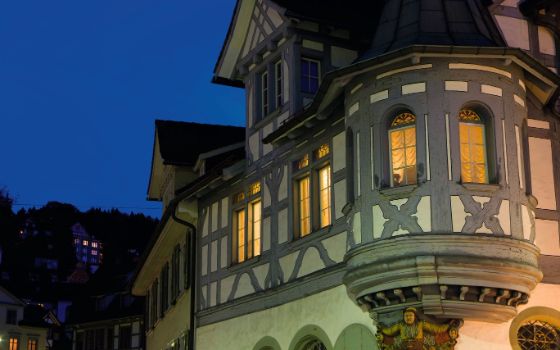 Beleuchteter Erker eines historischen Fachwerkhauses in der Altstadt von St. Gallen bei Abenddämmerung.