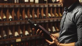 Mann betrachtet Weinflasche vor Regal mit edlen Weinen in Weinhandlung oder Vinothek