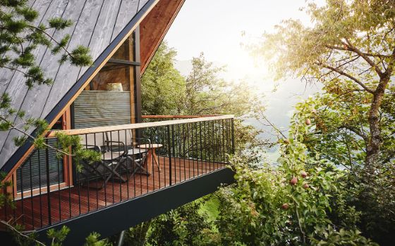 Moderne Eckterrasse eines Holzhauses in grünen Baumwipfeln.
