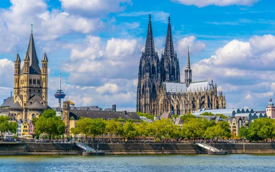 Panorama der Altstadt von Köln mit Dom hinter begrünter Uferpromenade vom Wasser aus. 