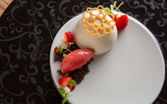 Auf einem schwarzen Teller ist eine weisse Mousse angerichtet mit Erdbeeren und einem kleinen Gebäck. 