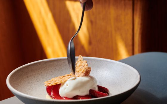 Ein Löffel sticht durch einen Keks, der auf einer weissen Mousse auf Erdbeeren angerichtet ist.