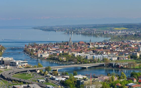 Panoramablick auf Konstanz am Bodensee mit Seerhein, Altstadt, Münster und mehreren Brücken, im Hintergrund die Schweizer Uferlandschaft.