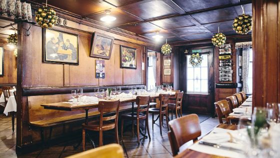 Ein rustikales Restaurant mit Holzstühlen und Tischen, an den Wänden hängen alte Ölgemälde.