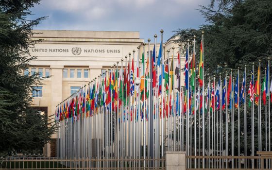 Palais des Nations in Genf mit Blick auf den Haupteingang und die Reihe internationaler Flaggen vor dem Gebäude.