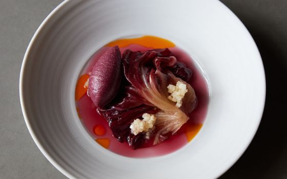 Aufsicht eines kunstvoll arrangierten Gerichtes mit Birne und Radicchio in roter Flüssigkeit auf einem weissen Teller auf grauem Untergrund.