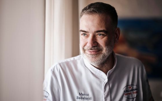 Das Bild zeigt den Küchenchef Marco Badalucci, eine Mann mit grauem Vollbart, blauen Augen und dunkelbraunen, kurzen Haaren, der lächelnd aus einem Fenster schaut. 