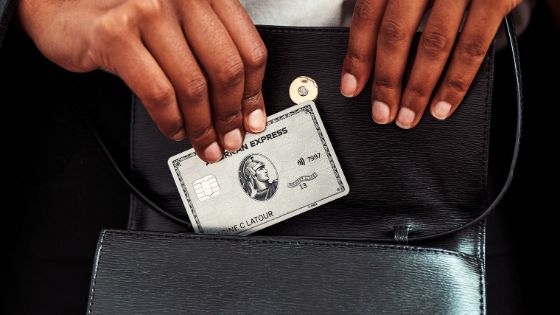 Nahaufnahme von zwei Händen mit einer silbernen Kreditkarte von American Express an der Innenseite einer aufgeklappten, schwarzen Lederhandtasche.