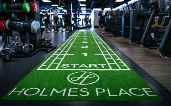 Trainingsfläche in einem Fitnessstudio mit einer grünen Matte mit Metermarkierungen und dem Aufdruck Holmes Place.