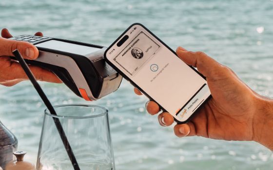 Mobile Payment per Smartphone mit einer silbernen Kreditkarte von American Express auf dem Display an einem Kartenlesegerät an einem Tisch am Wasser bei Sonnenschein