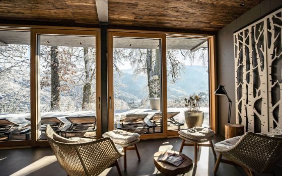 Lounge-Stühle stehen in einem gemütlichen Raum mit bodentiefen Fenstern, die Aussicht zeigt Berge mit Schnee.