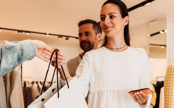 Ein Paar beim Einkauf in einer Modeboutique, sie nimmt lächelnd eine Einkaufstüte entgegen. 