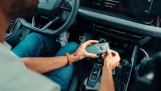 Blick auf die Mittelkonsole eines schicken Autos, wo Hände eine Kreditkarte von American Express aus einem schmalen Leder-Kartenhalter ziehen