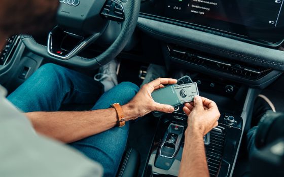 Blick auf die Mittelkonsole eines schicken Autos, wo Hände eine Kreditkarte von American Express aus einem schmalen Leder-Kartenhalter ziehen