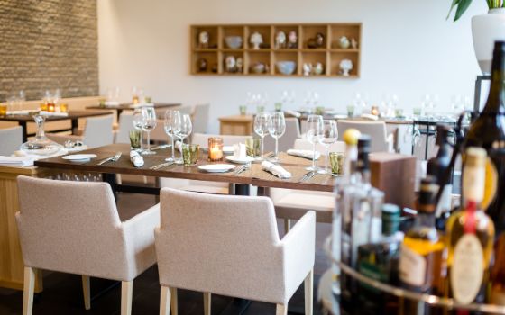 Innenraum eines Restaurants mit mehreren eingedeckten Tischgruppen und weissen Polsterstühlen.